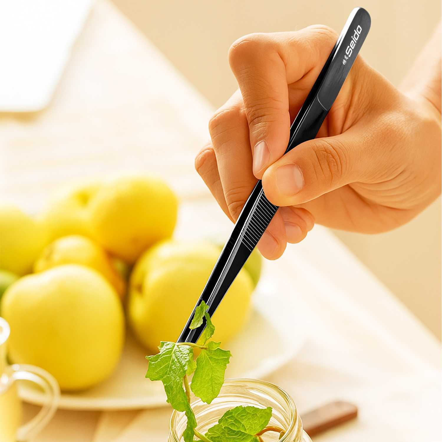 Hand holding a black straight tweezer with herbs, surrounded by lemons on a light background.