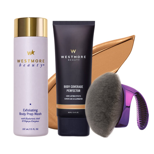 Westmore Beauty hair and skin care set featuring Exfoliating Body Prep Wash in a lavender bottle with a gold cap, Body Coverage Perfector in a dark navy tube with a gold band, a large gold makeup brush, a gray bristle brush, and a purple-to-clear facial cleansing device, all on a white background.