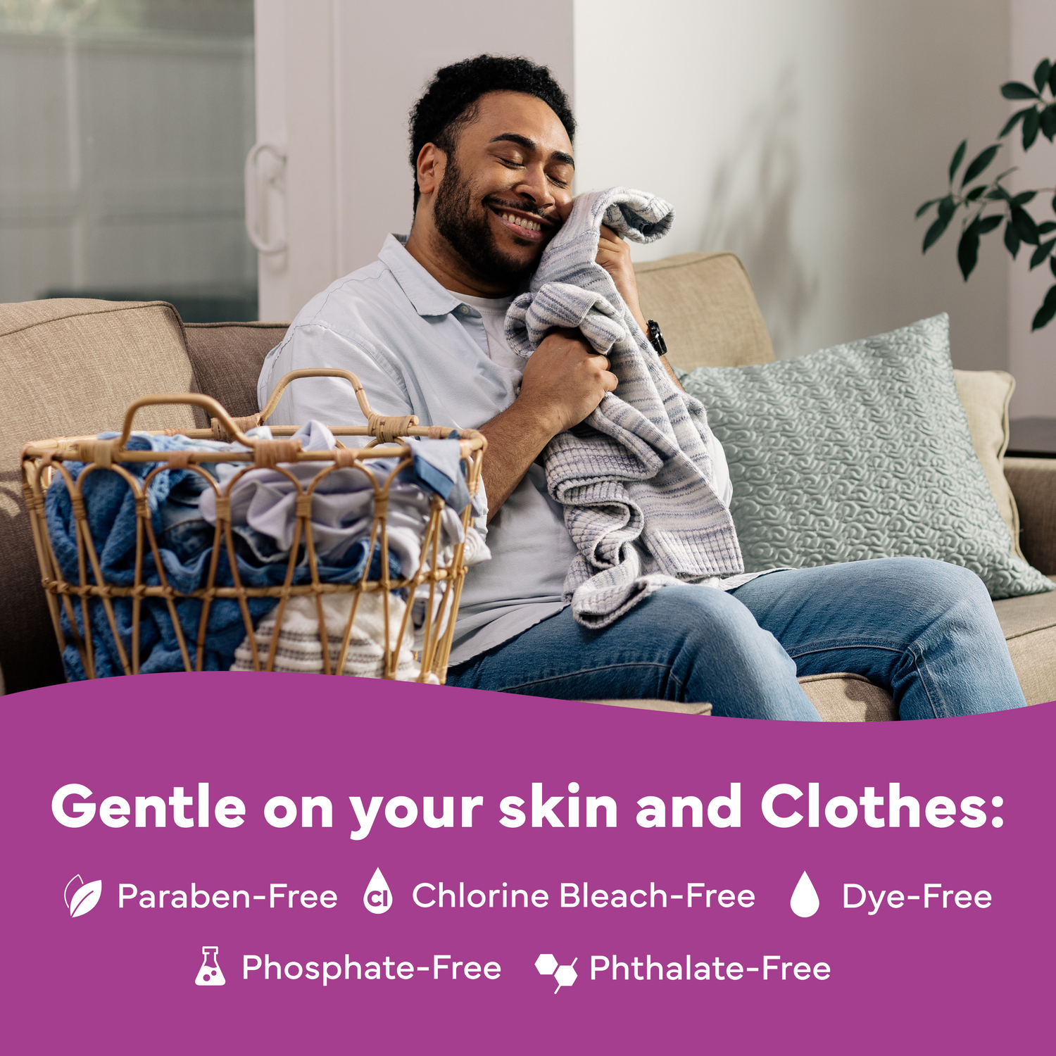 Man sitting on a couch with a basket of laundry, holding a towel, in a home setting.