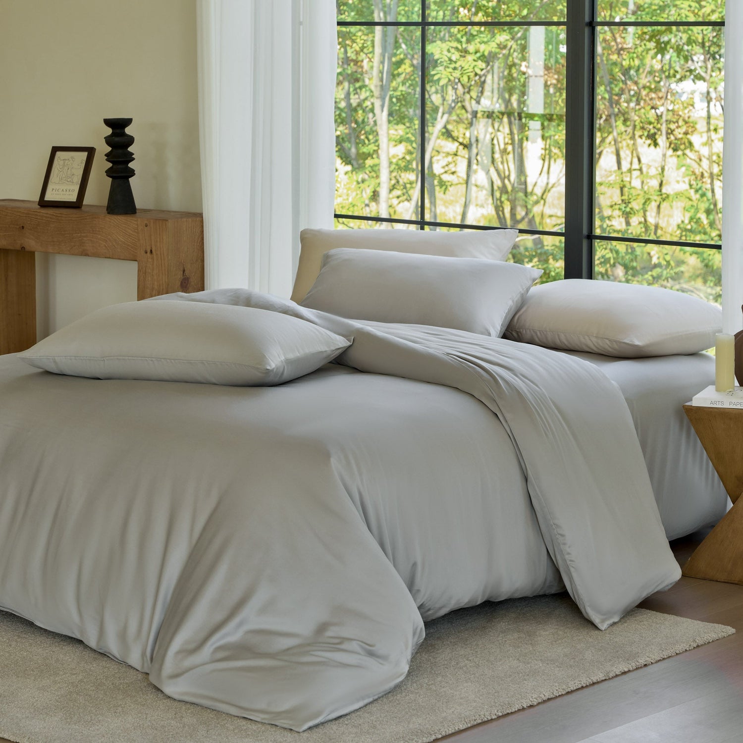 Neatly made bed with beige bedding in a room with large windows.