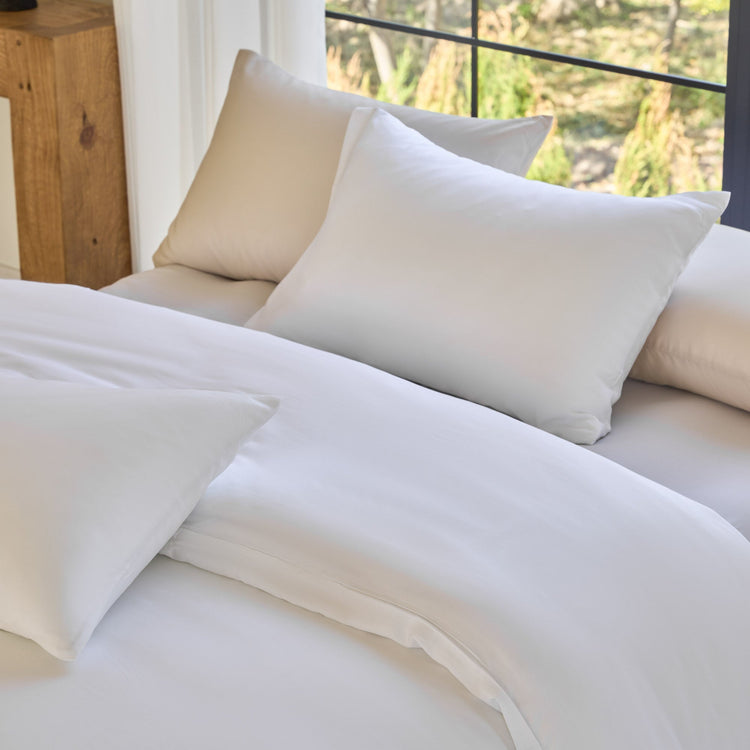 White bedding set with pillows on a bed in a bright room.