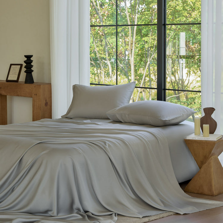 Neatly made bed with beige bedding in a bright room with large windows.