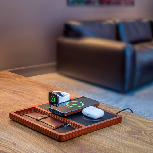 A wireless charging pad with integrated Apple Watch charger, featuring a black and oak design, with a smartphone, smartwatch, and earbuds being charged.