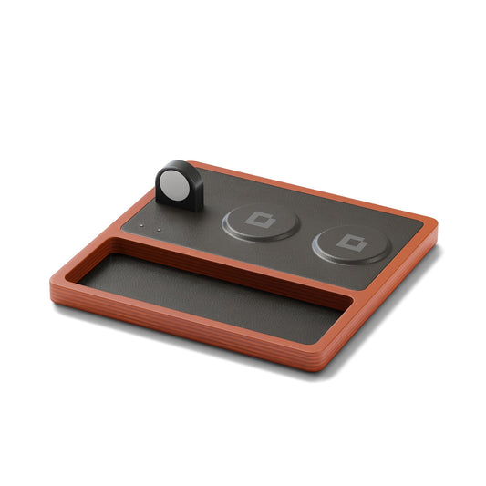 A wireless charging pad with integrated Apple Watch charger, featuring a black and oak design, with a smartphone, smartwatch, and earbuds being charged.