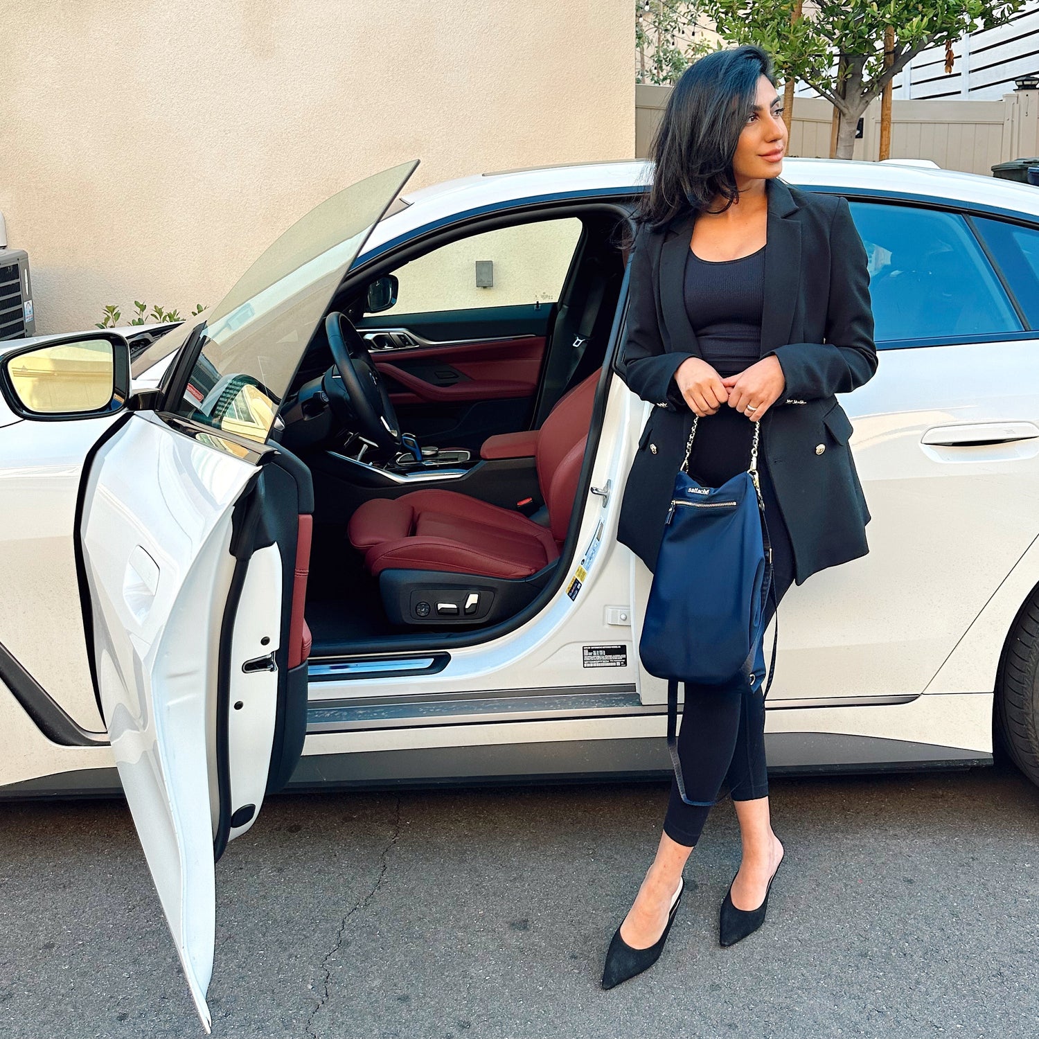Woman standing next to a white car with open door, wearing a black outfit.