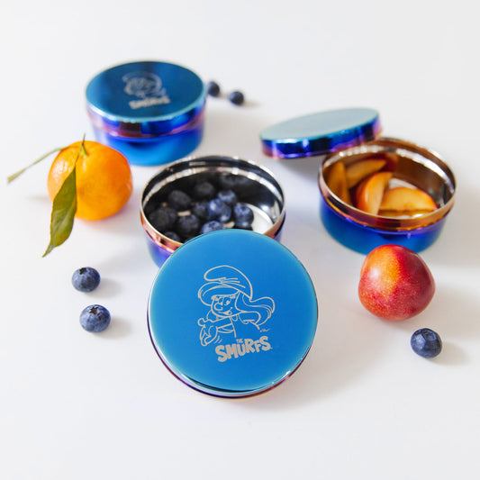 Three blue metal containers with colorful rims on a white background - each with a Smurf etched on the lid along with The Smurfs logo - Papa Smurf, Smurfette, and Classic Smurf