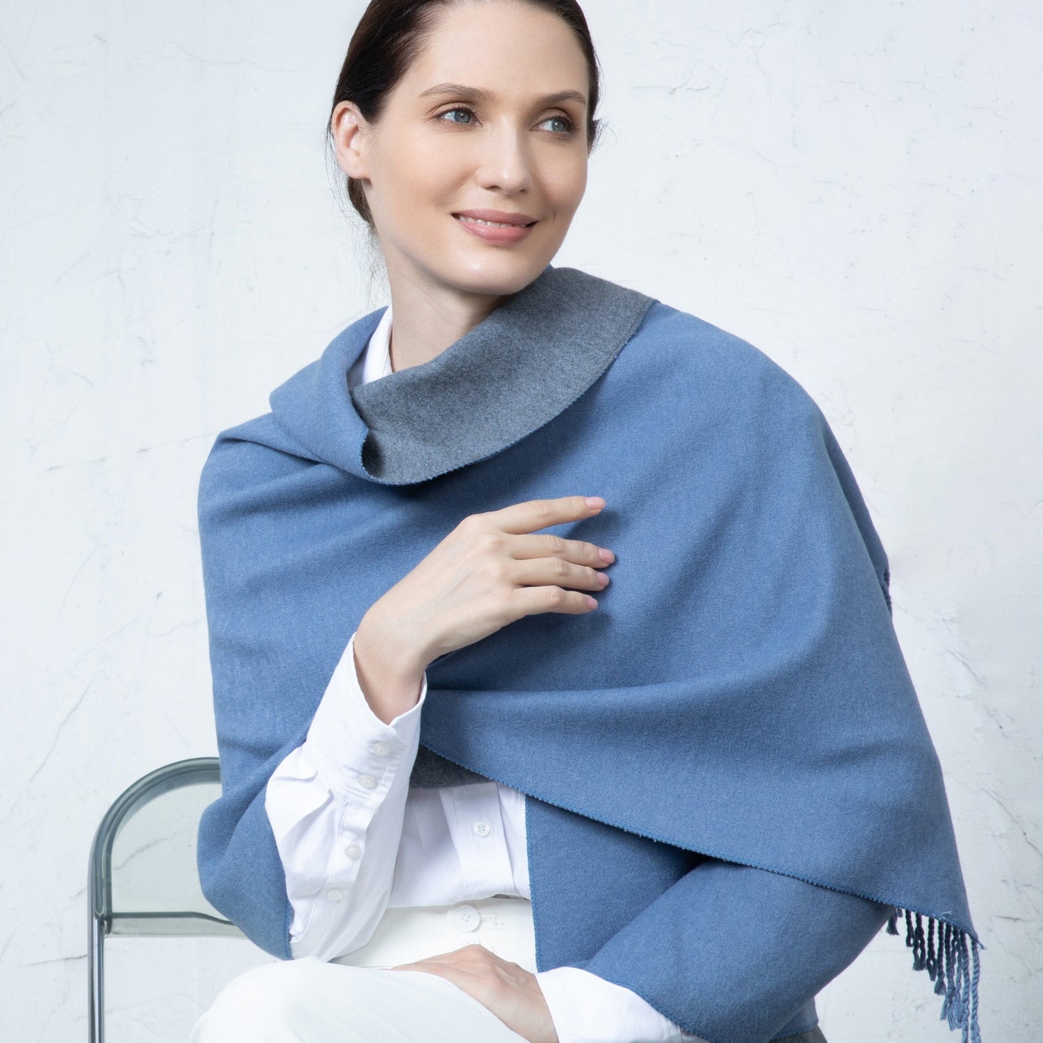 Woman wearing a blue shawl over a white outfit against a light gray background