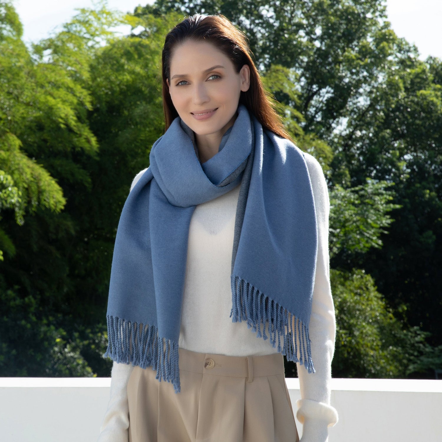 Woman wearing a blue scarf outdoors with green trees in the background