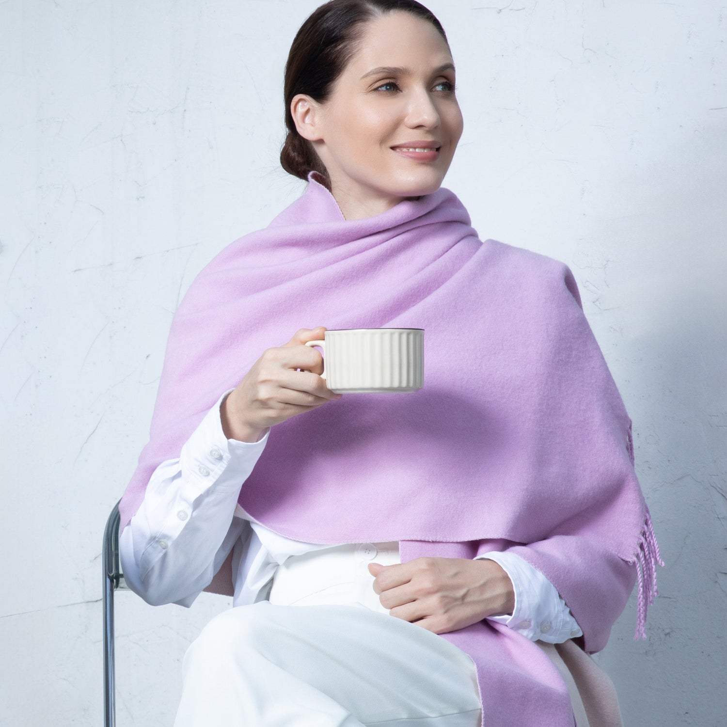 Woman wearing a light purple scarf holding a white mug against a plain background