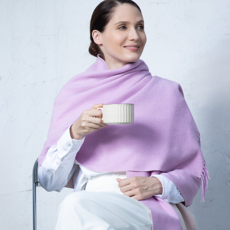 Woman wearing a light purple scarf holding a white mug against a plain background