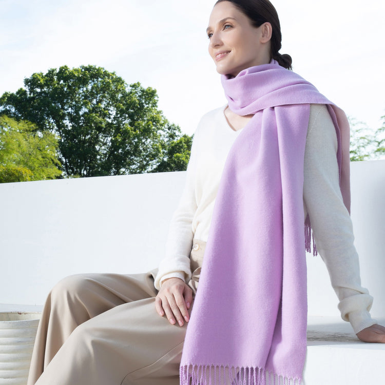 Woman wearing a light purple scarf sitting outdoors with trees in the background
