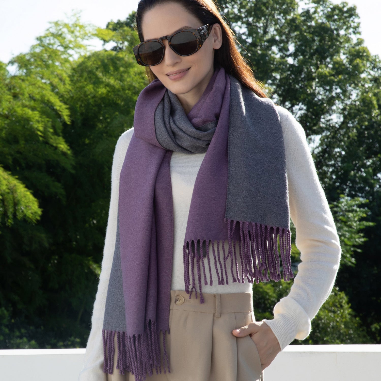 Woman wearing a purple and gray scarf outdoors with green trees in the background
