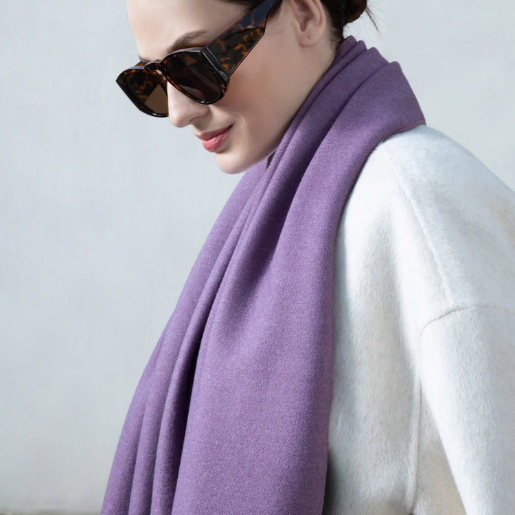 Person wearing a purple scarf and sunglasses against a plain background