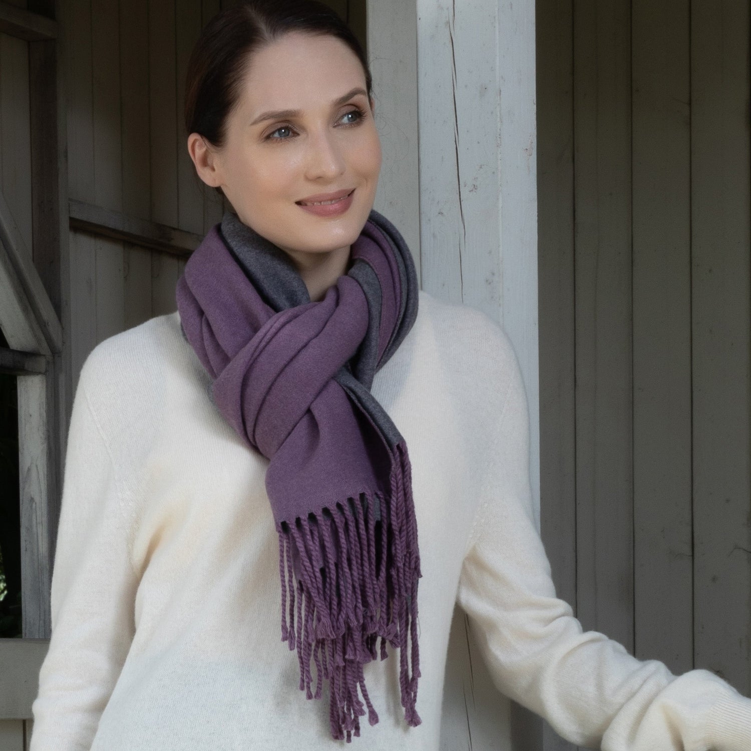 Woman wearing a purple scarf and white sweater standing against a wooden wall.