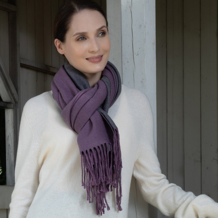 Woman wearing a purple scarf and white sweater standing against a wooden wall.