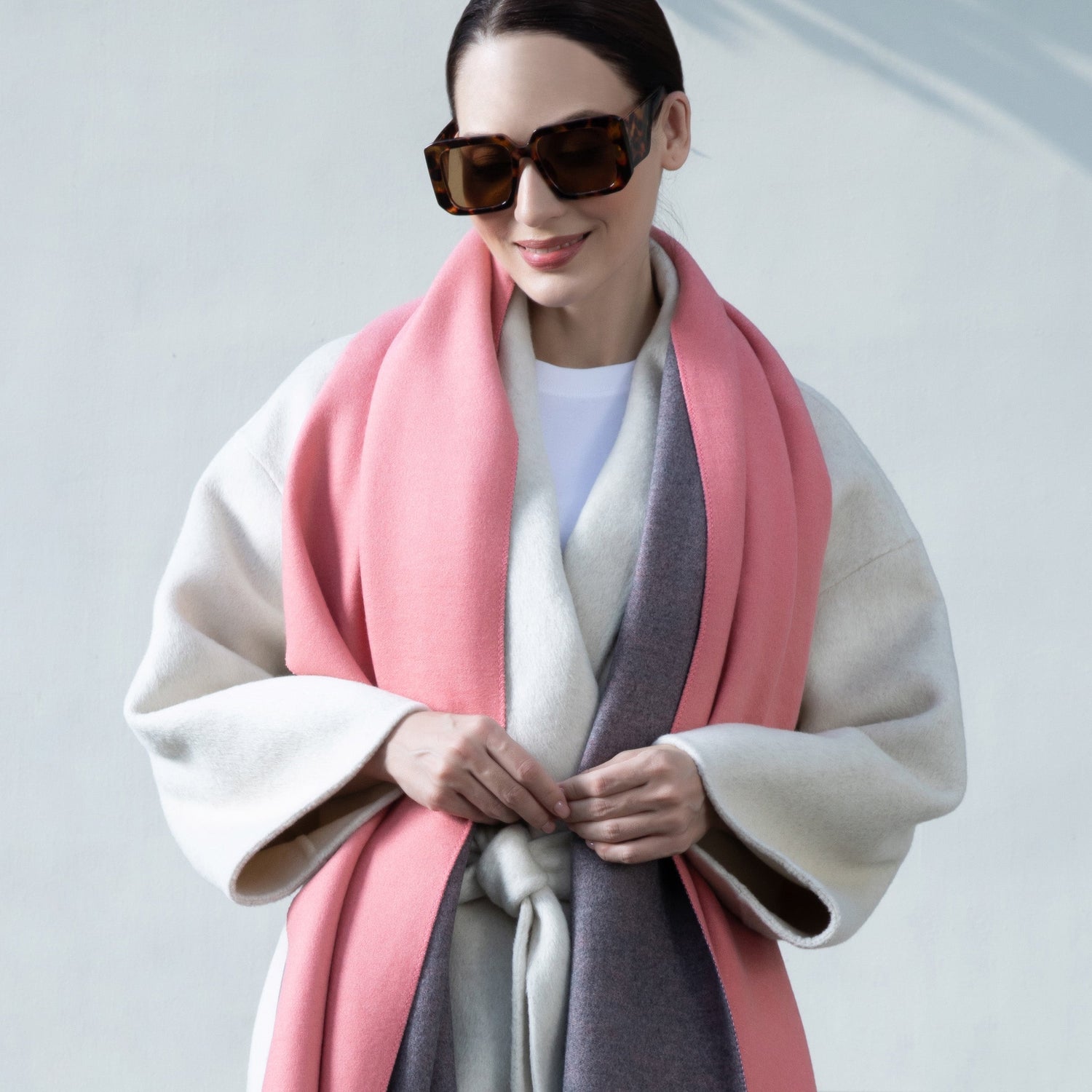 Woman wearing a pink and gray scarf with sunglasses on a light background