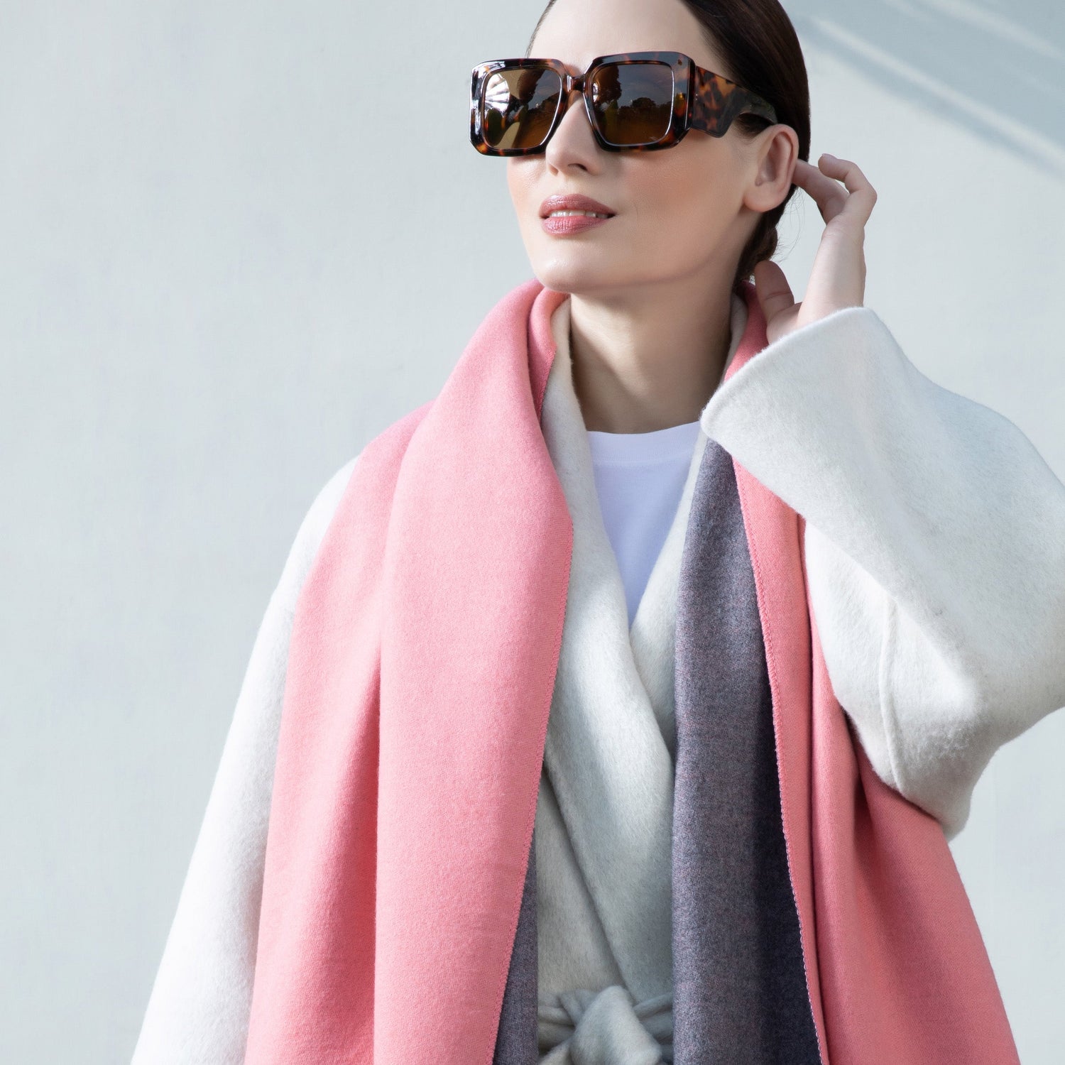 Woman wearing a pink scarf and sunglasses against a light gray background