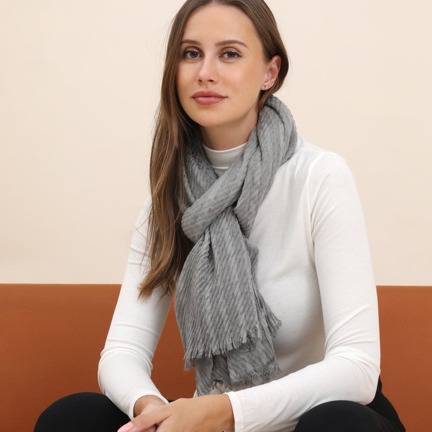 Woman wearing a gray scarf sitting on a brown couch with a beige wall background