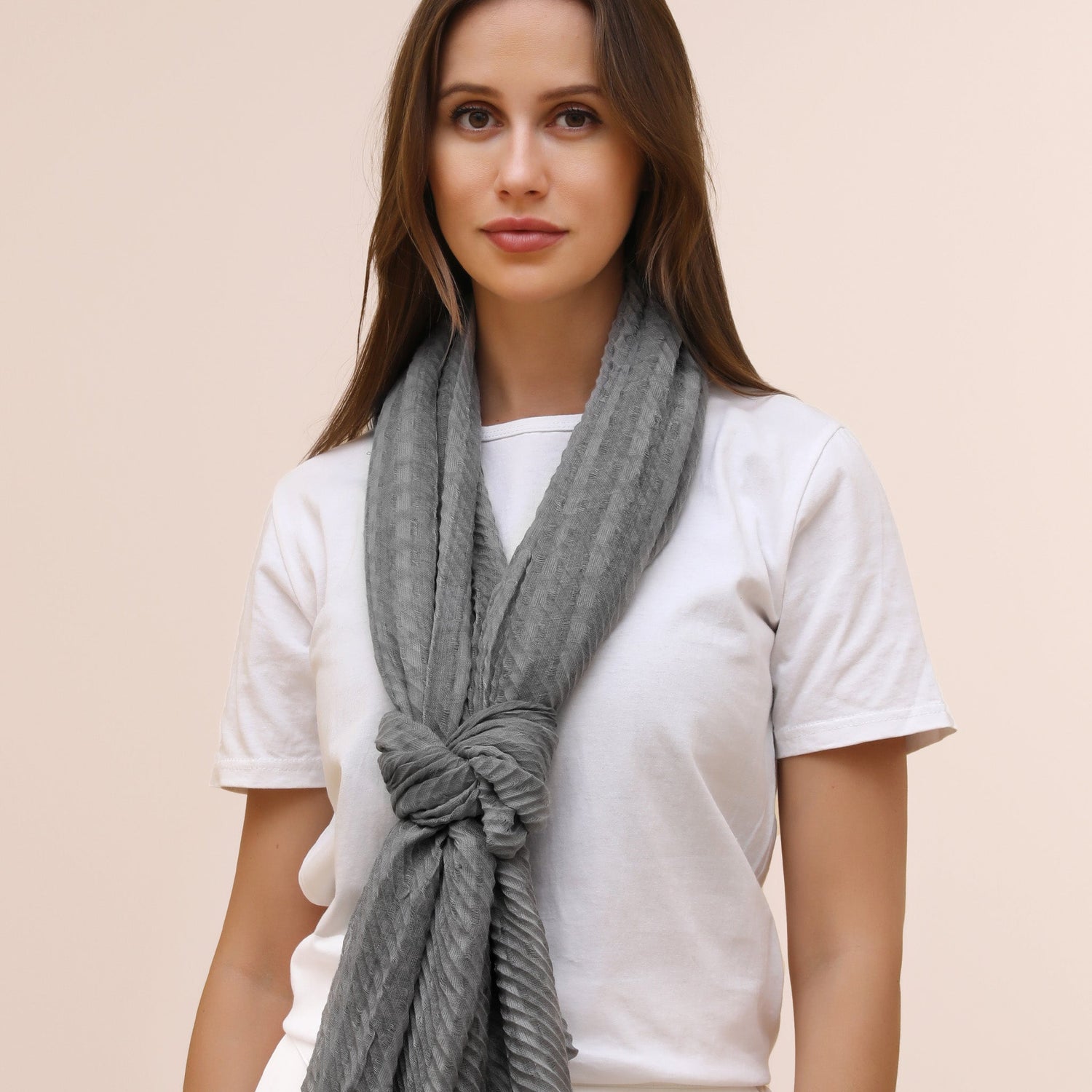Woman wearing a gray scarf around her neck against a beige background