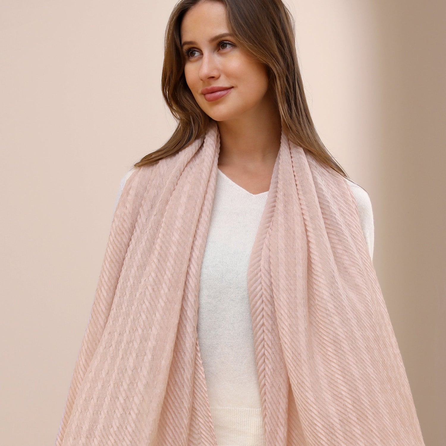 A woman wearing a lightweight blue and white striped scarf around her neck, with a white top and dark pants, sitting against a neutral background.