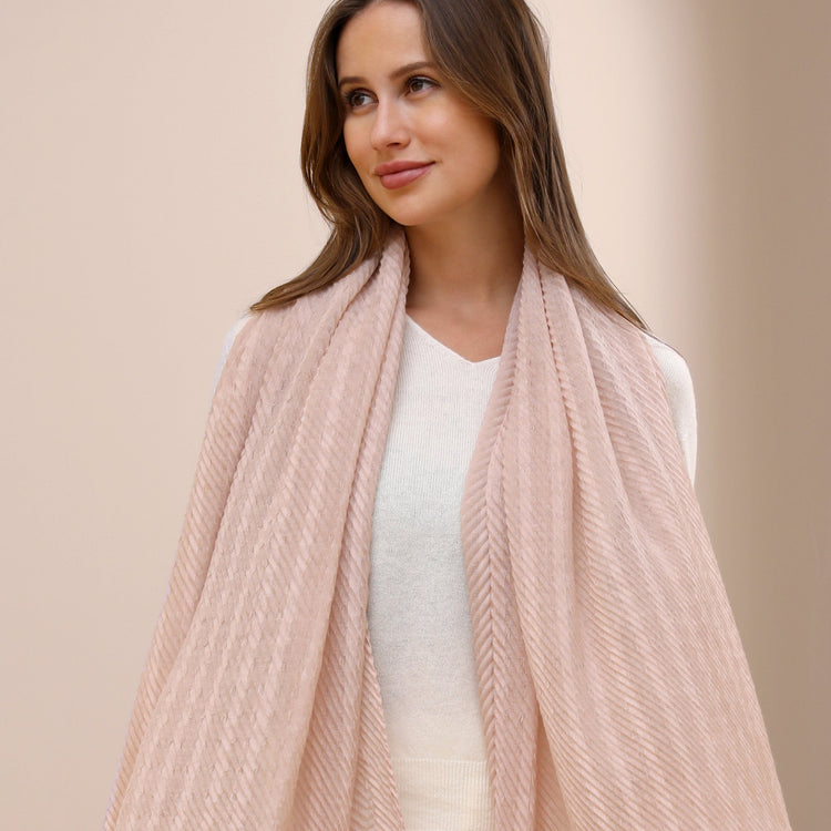 A woman wearing a lightweight blue and white striped scarf around her neck, with a white top and dark pants, sitting against a neutral background.