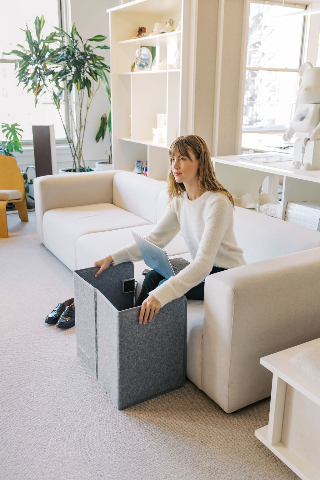 Woman sitting on a white sofa in a bright living room with a gray storage cube.