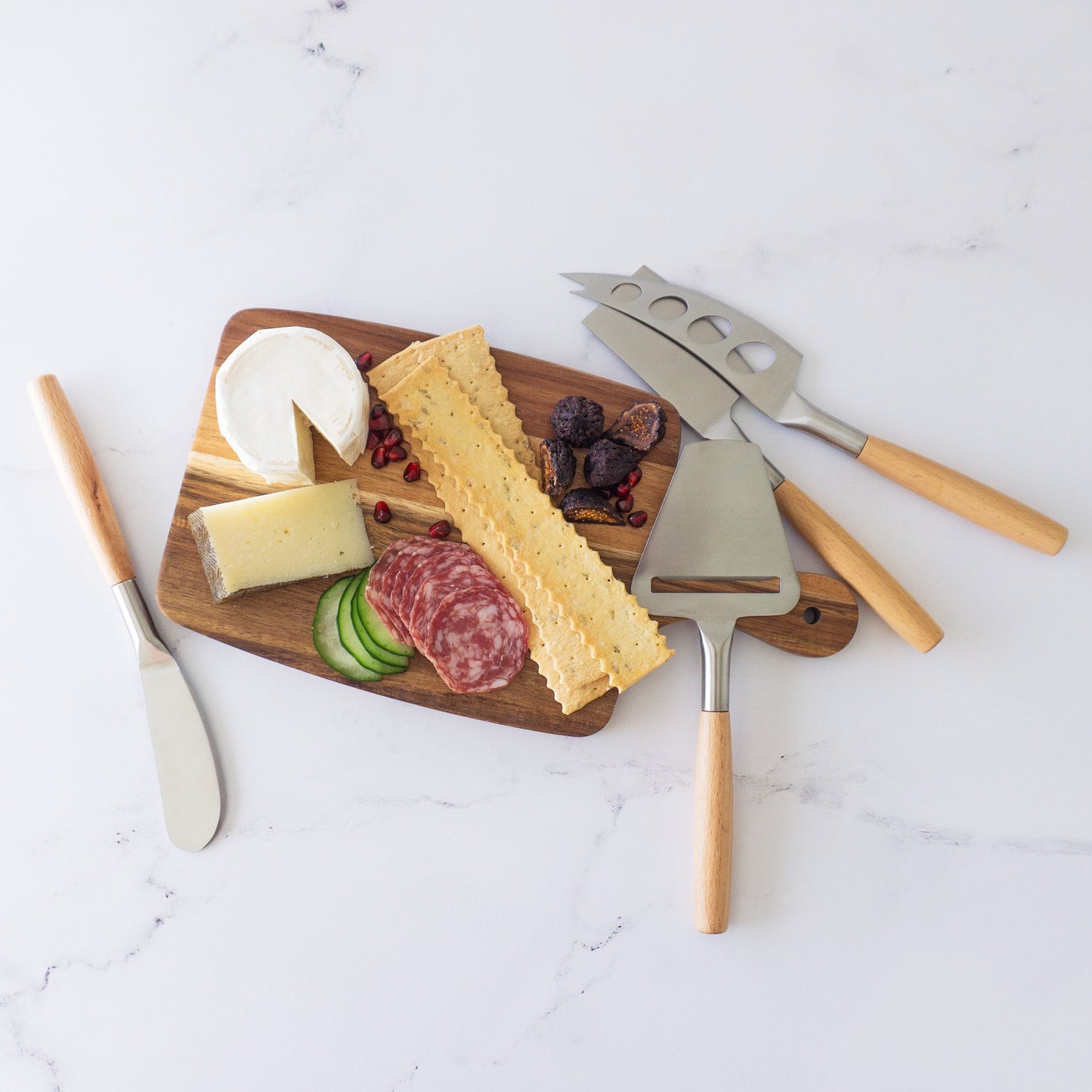 Wooden board with cheese, salami, and crackers on a marble surface with cheese tools.