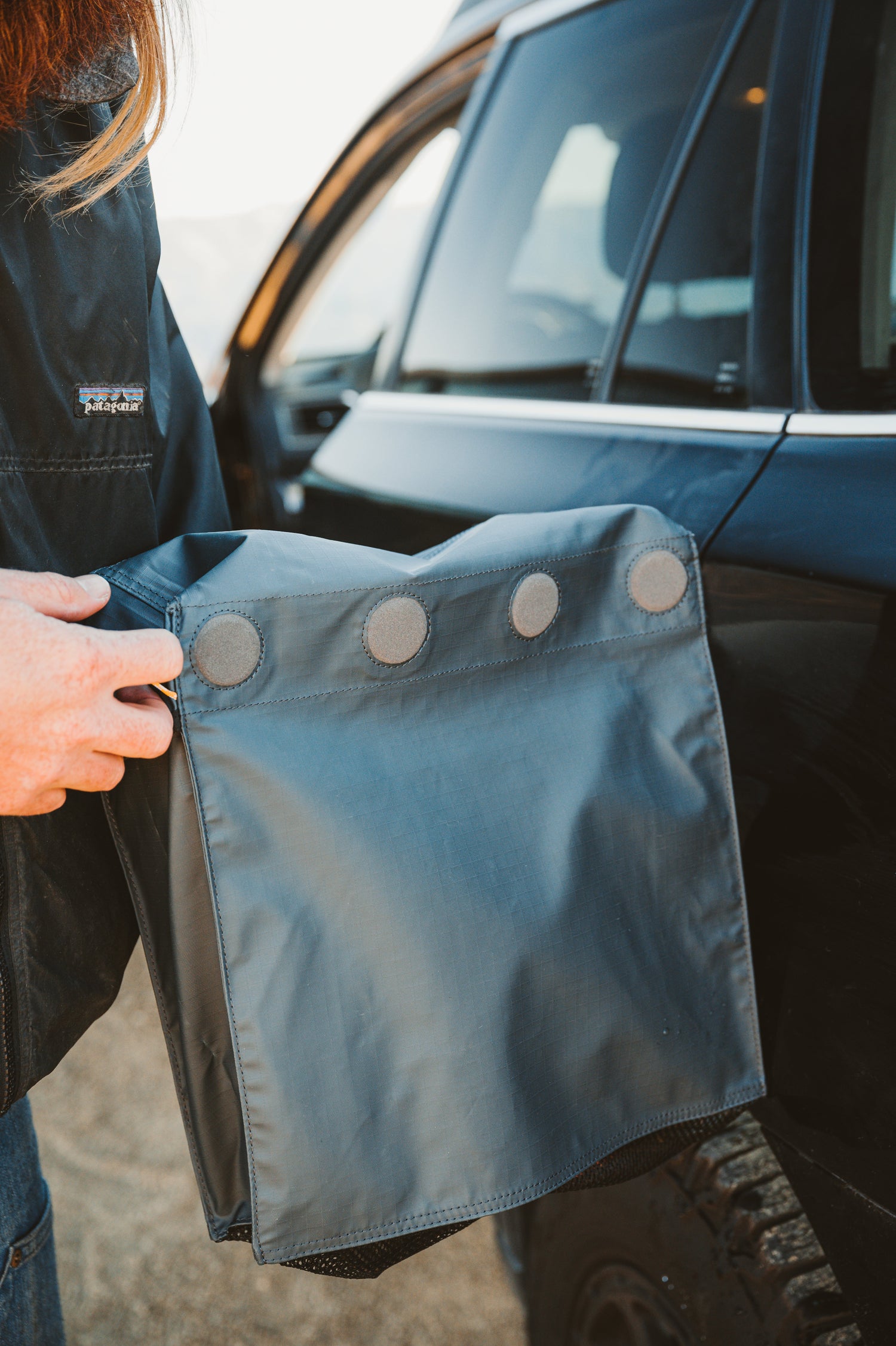 Person holding a blue car boot liner with buttons near a vehicle