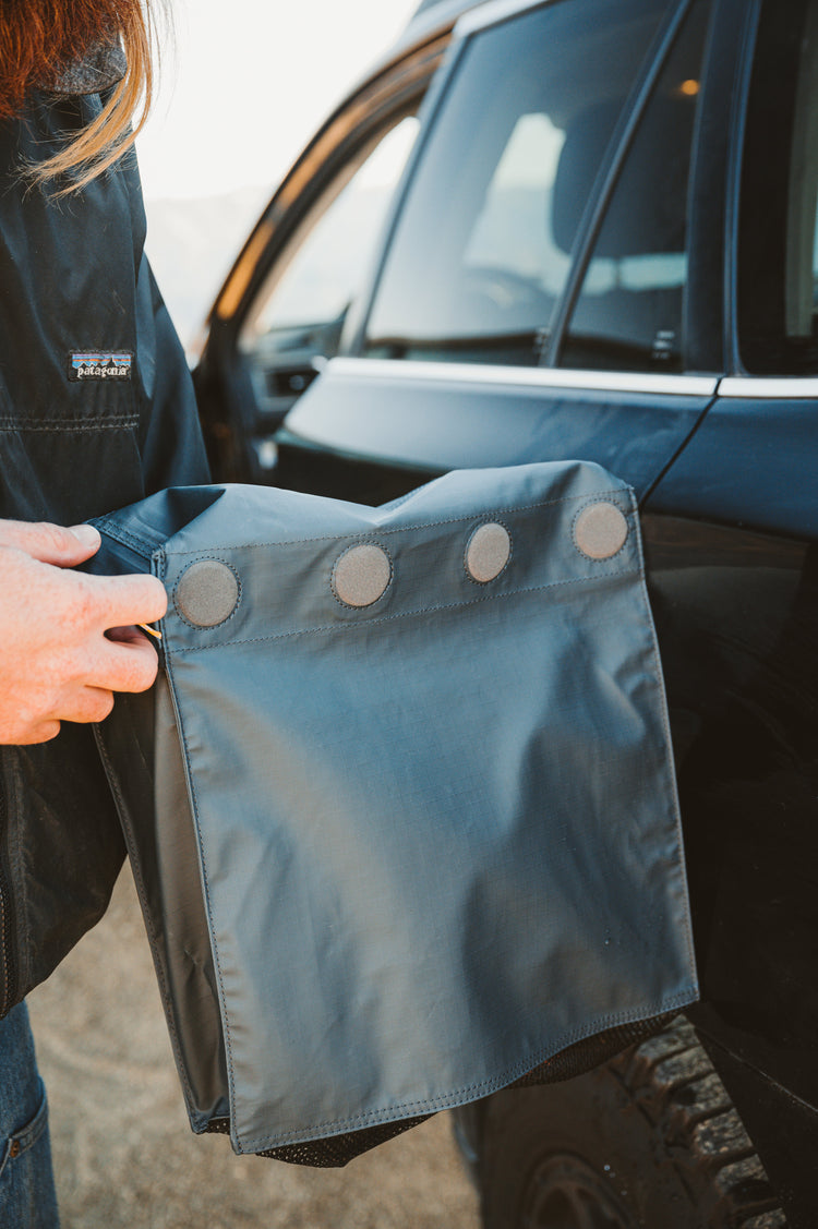 Person holding a blue car boot liner with buttons near a vehicle