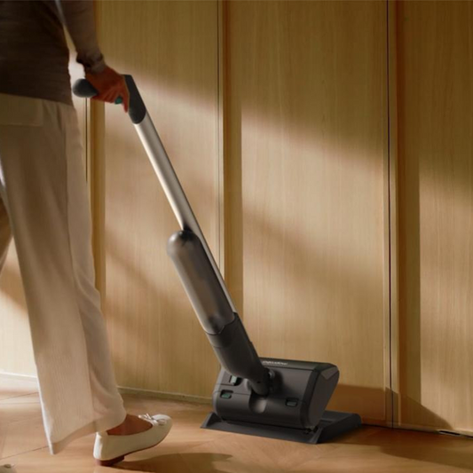Person using a vacuum cleaner on a wooden floor in a kitchen.