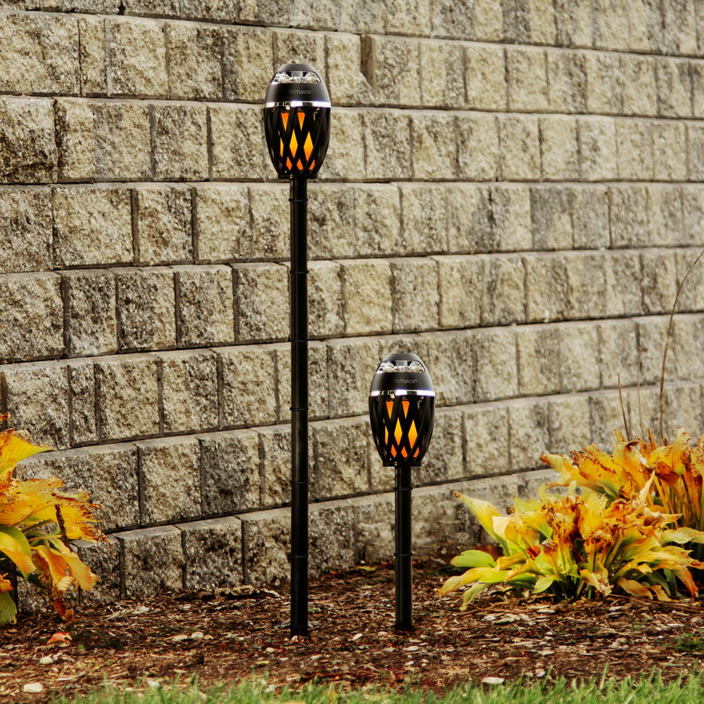 Two solar-powered garden lights against a stone wall with plants in the foreground.