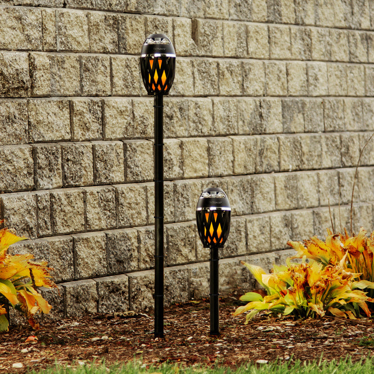 Two solar-powered garden lights against a stone wall with plants in the foreground.