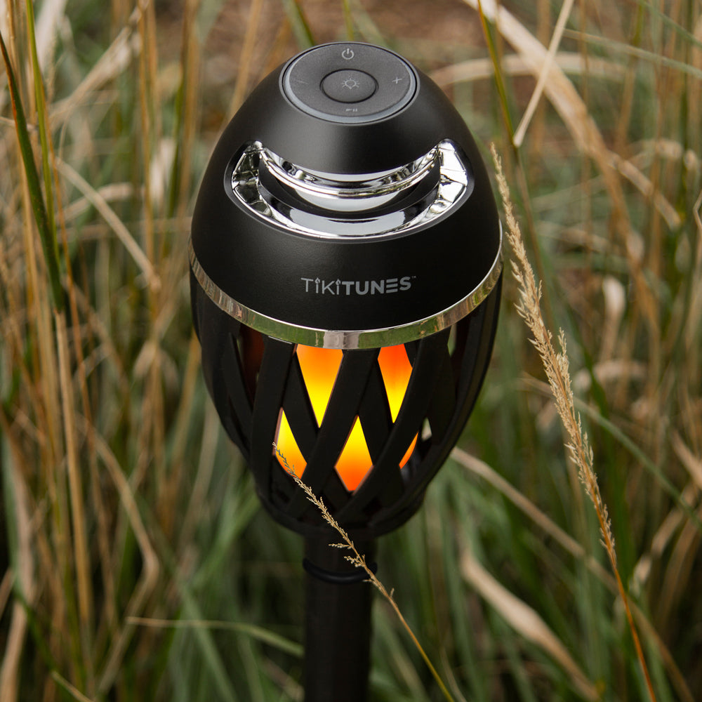 Black TikiTunes speaker with flame-like design in a grassy setting