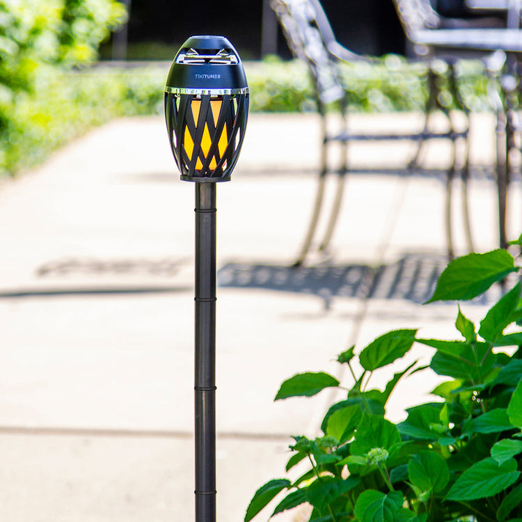 Solar-powered outdoor lamp on a garden path with plants and furniture in the background