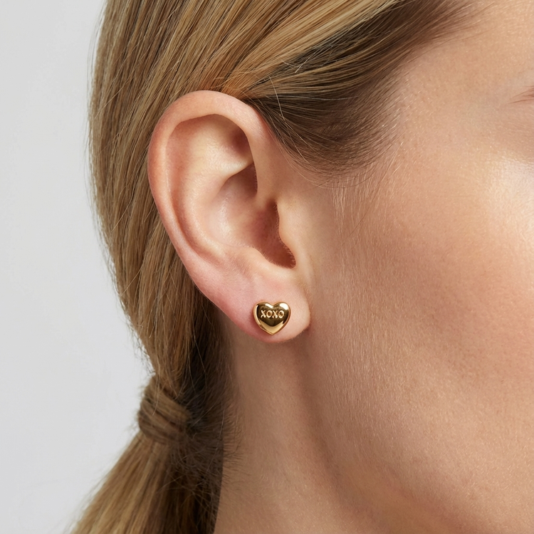 Gold heart-shaped earring worn by a person with a plain background