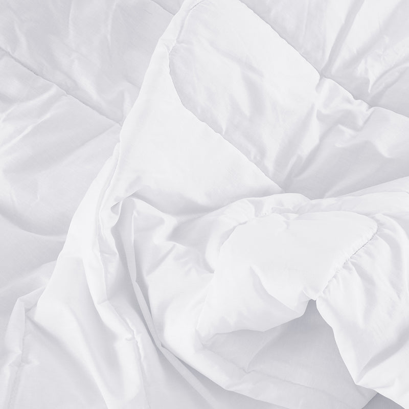 Close-up of a white quilted comforter with folds on a white background
