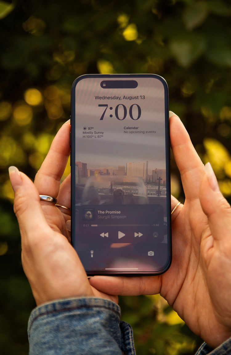 Person holding a smartphone with a music player app on a blurred natural background