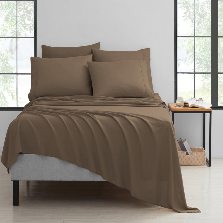Brown bedspread set on a bed in a room with large windows.