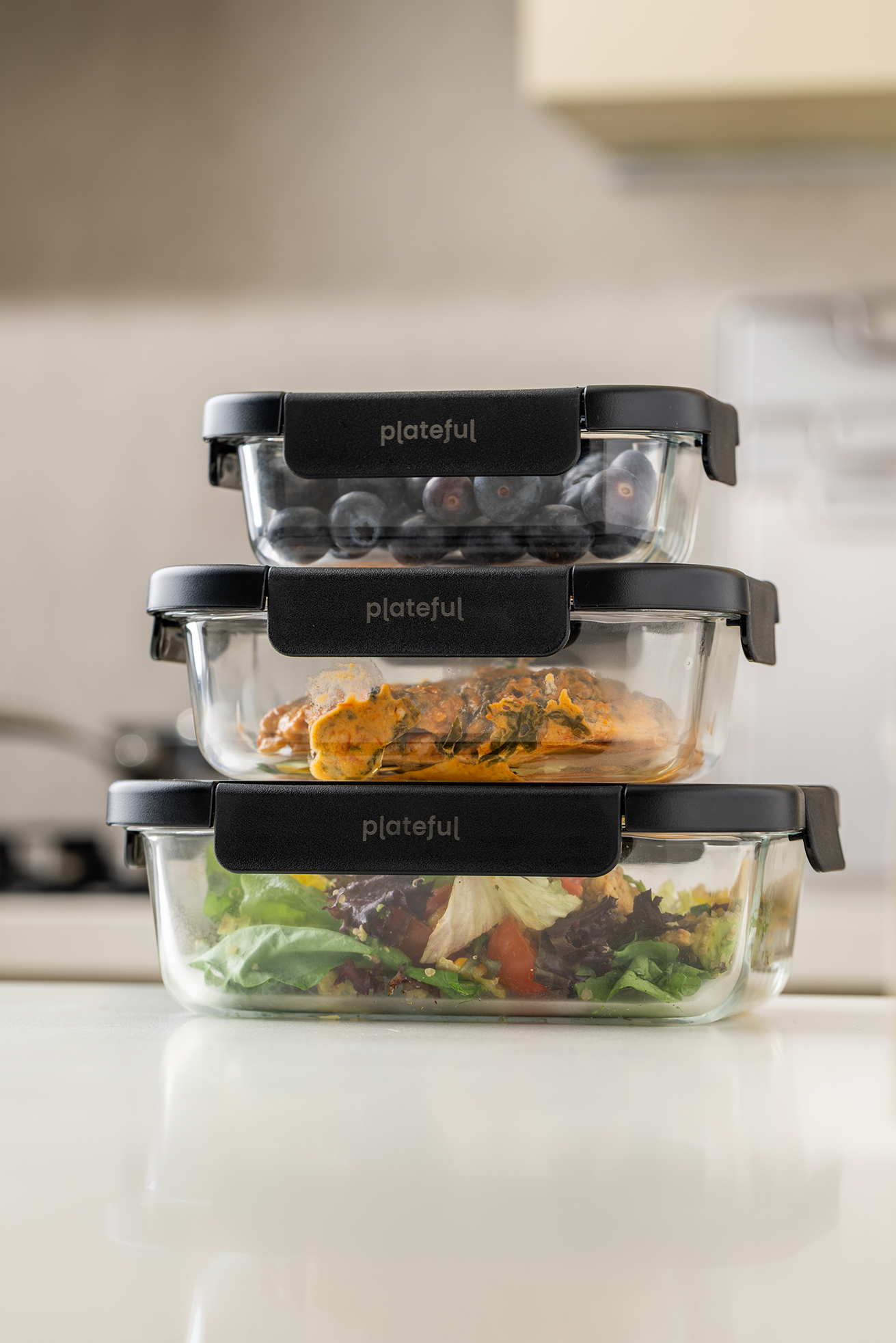 Set of glass food storage containers with black lids on a kitchen counter.