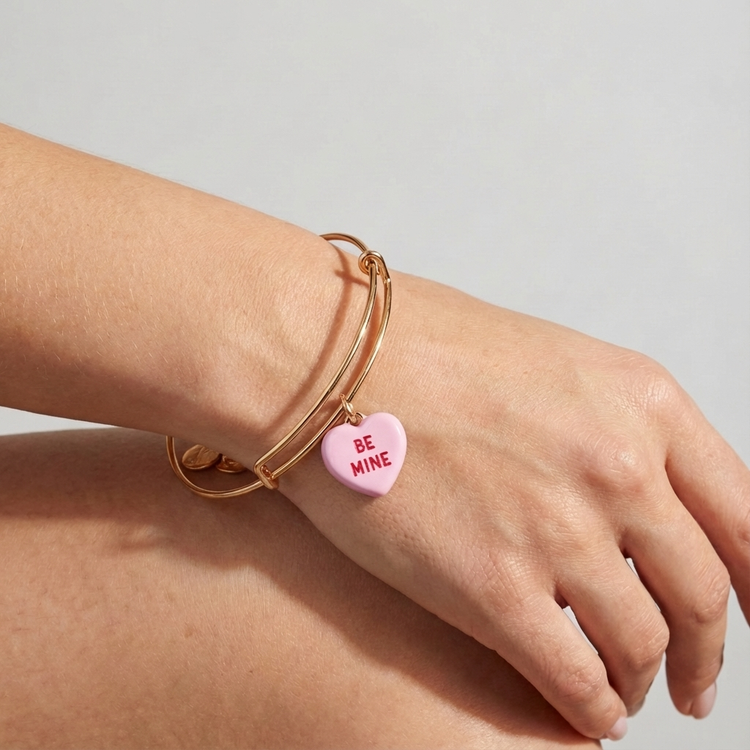 Gold bracelet with a pink heart-shaped charm on a light gray background