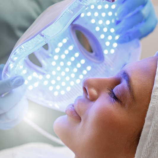 A LED light therapy facial mask and a bottle of high energy hyaluronic serum, both branded by Pure Daily Care, with the mask illustrated in a rainbow of light colors and the serum bottle labeled.