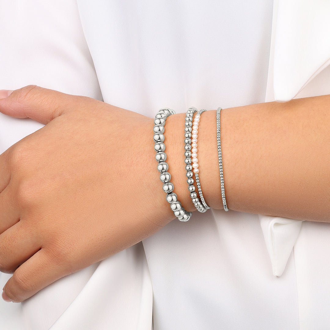 Close-up of a wrist wearing multiple silver beaded bracelets on a white background