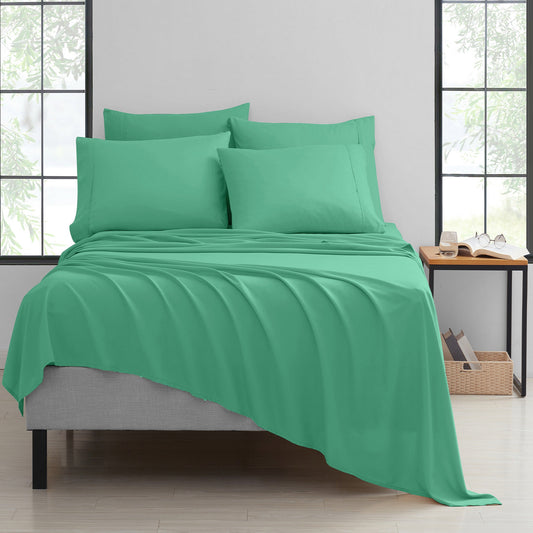 Green bedspread set on a bed in a room with large windows.