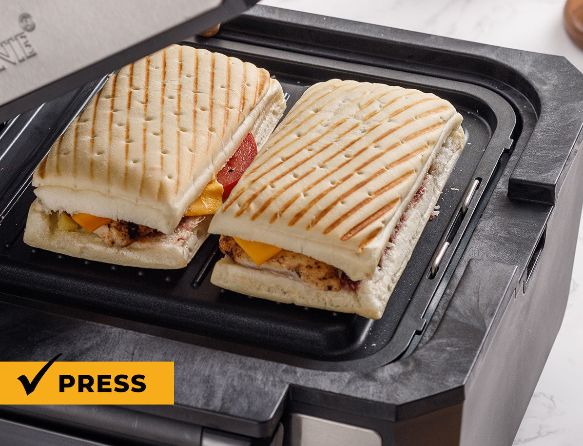 Two grilled sandwiches on a panini press with 'Press' button visible.