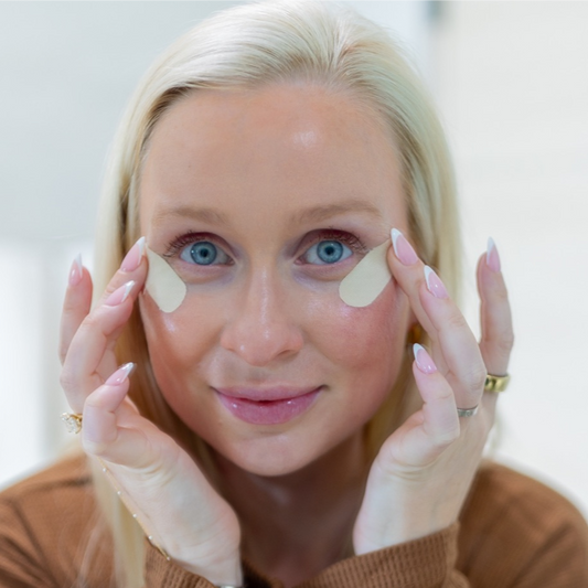 Woman applying eye patches with a neutral background
