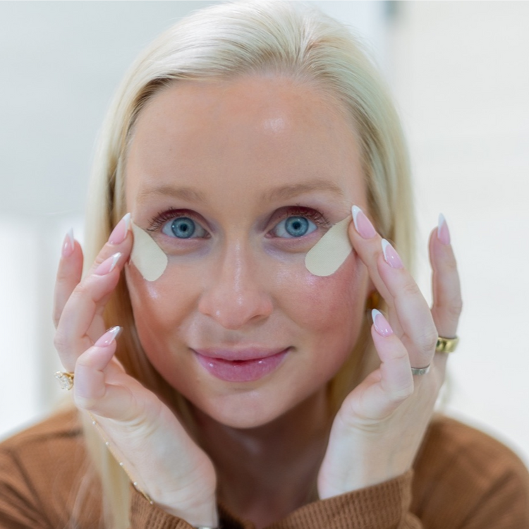 Woman applying eye patches with a neutral background