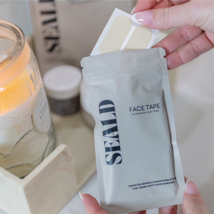 Hand holding a package of 'SEALD' face tape with a candle in the background