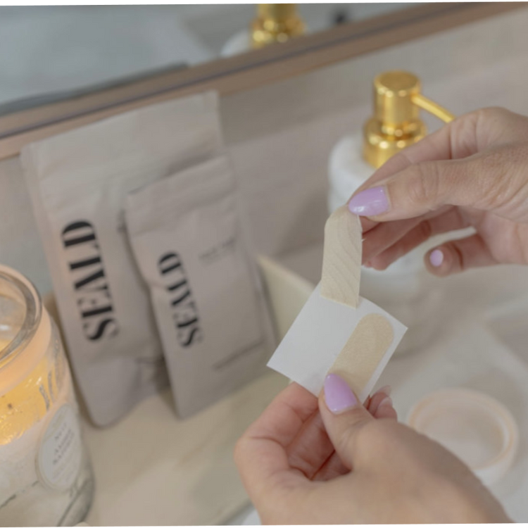 Person holding a seald face tape over a sink with a candle and seald packaging in the background