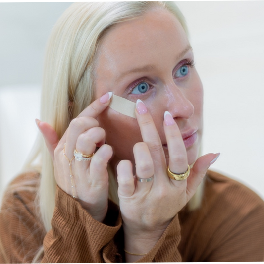 Woman applying eye patches with a neutral background