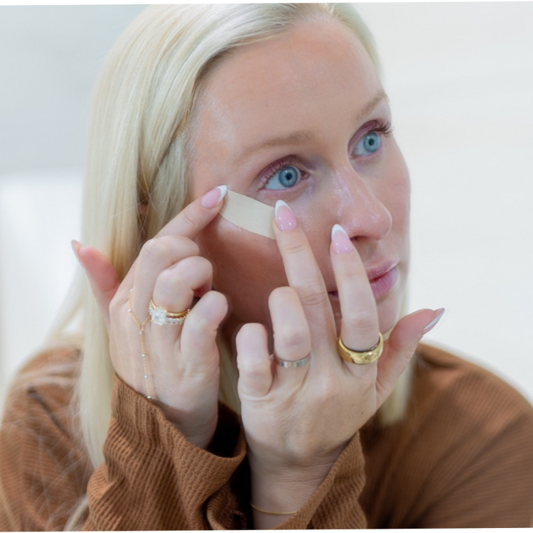 Woman applying a seald face tape to her face with a white background